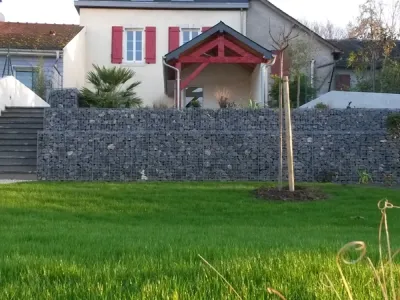 Jardin aménagé avec mur de soutènement en gabions, pelouse naturelle et plantations devant une maison individuelle