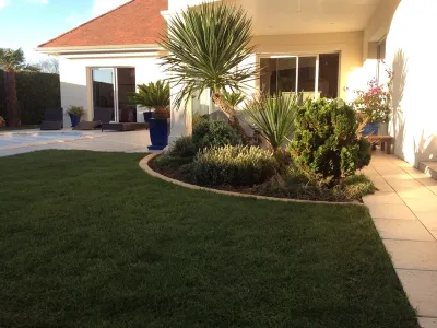Jardin paysager avec massifs végétalisés et pelouse soignée autour d’une maison