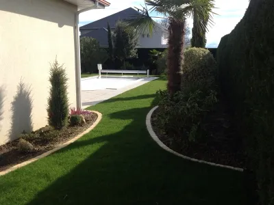 Allée verte avec pelouse et plantations le long de la maison dans un jardin paysager