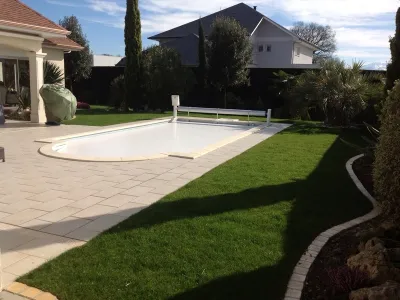 Jardin aménagé avec piscine, terrasse minérale et pelouse soignée autour de la maison