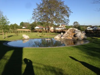 Vue d’ensemble d’un bassin de jardin aménagé avec pelouse et roches naturelles